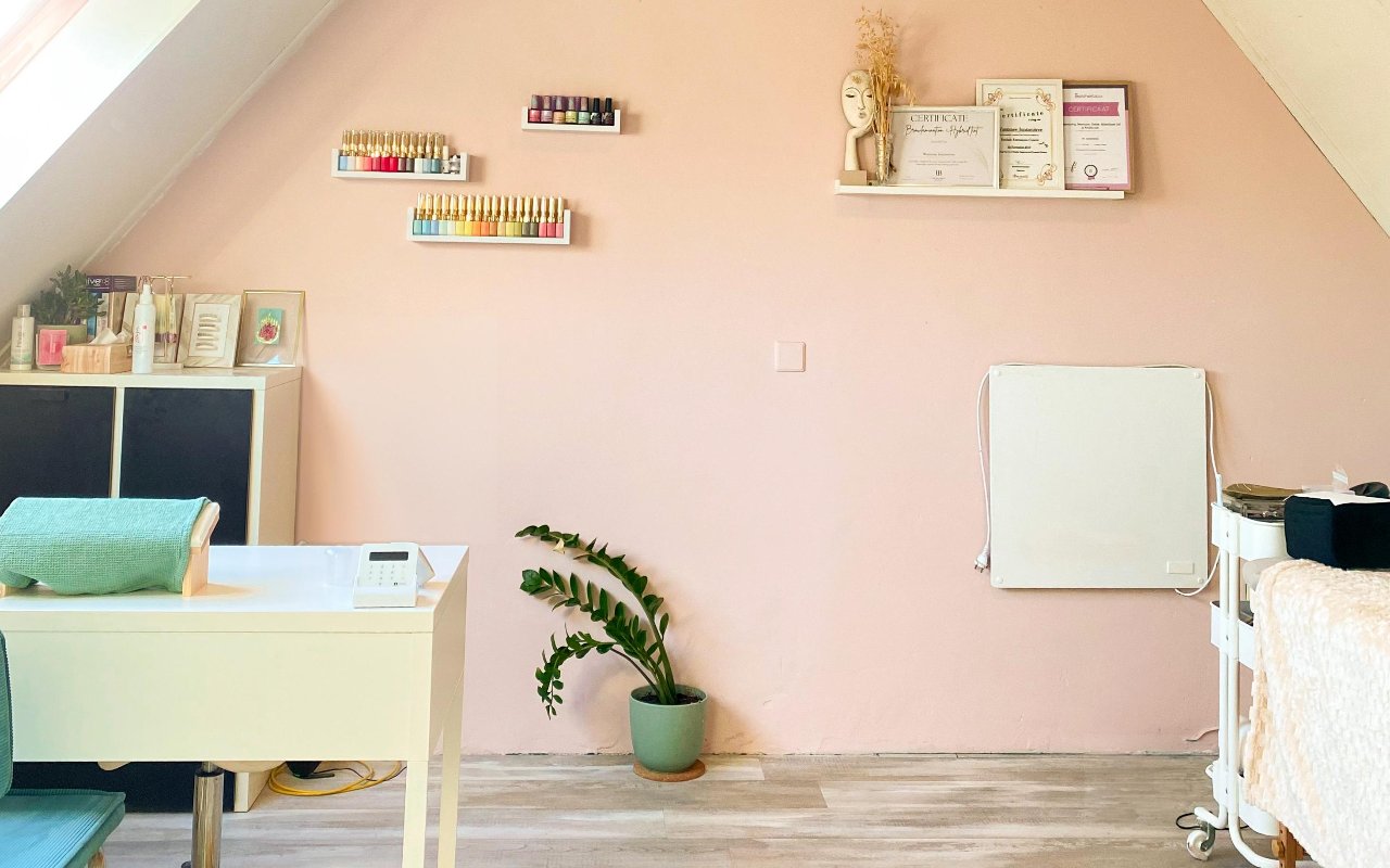 De studio met de roze wand, planken met gellak en het bureau